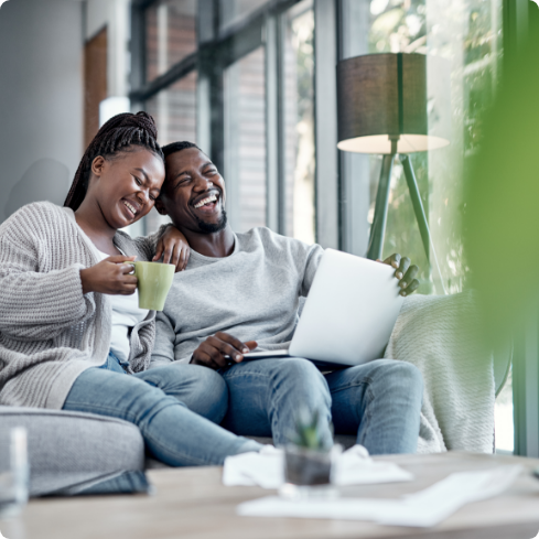 Women holding coffee cup and men holding laptop sitting on a couch laughing