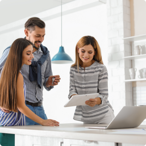 A Couple standing together holding a key and a seller showing them something over notepad.